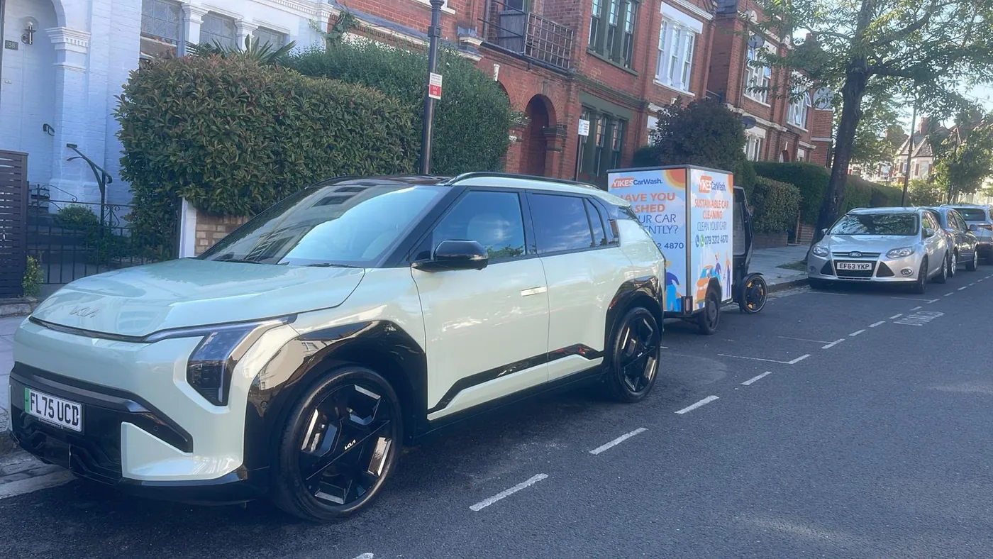 Yikes cargo e-bike washing a Kia EV3 parked on a residential London street