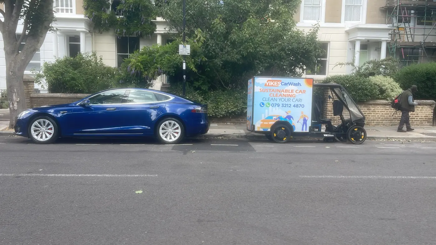Yikes cargo e-bike unit behind a blue Tesla Model S on a leafy street, set up for paintwork