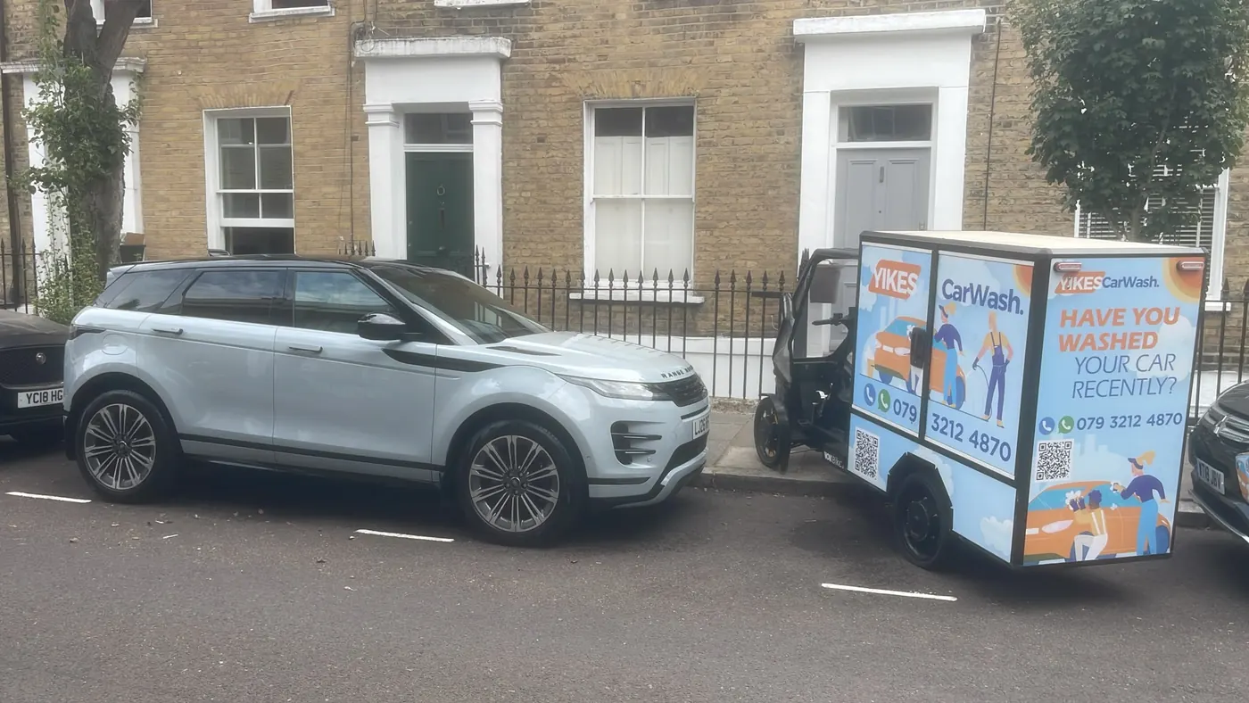 Yikes cargo e-bike trailer arriving for a mobile car wash behind a Range Rover Evoque parked at the kerb of a terraced London street