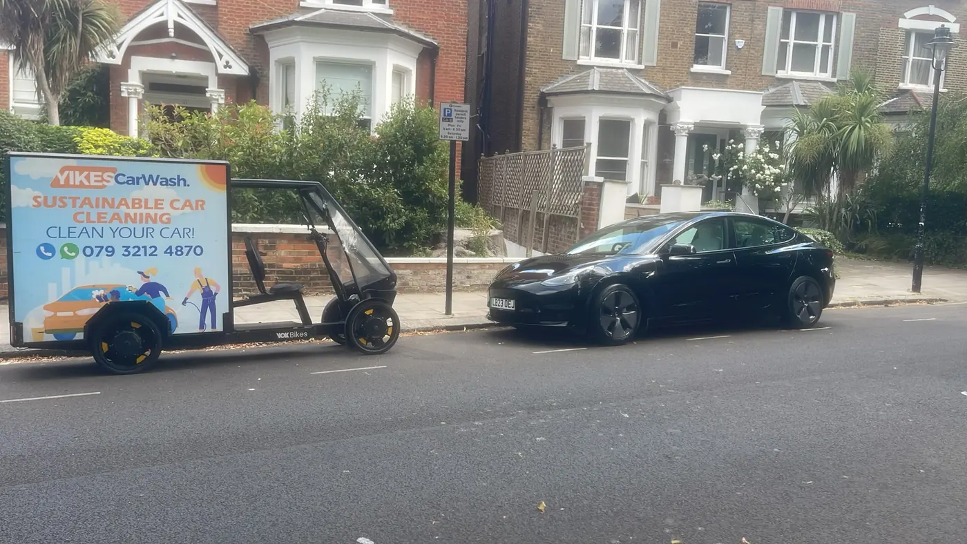 Yikes cargo e-bike trailer set up for mobile valeting beside a black Tesla Model 3 in a resident permit bay
